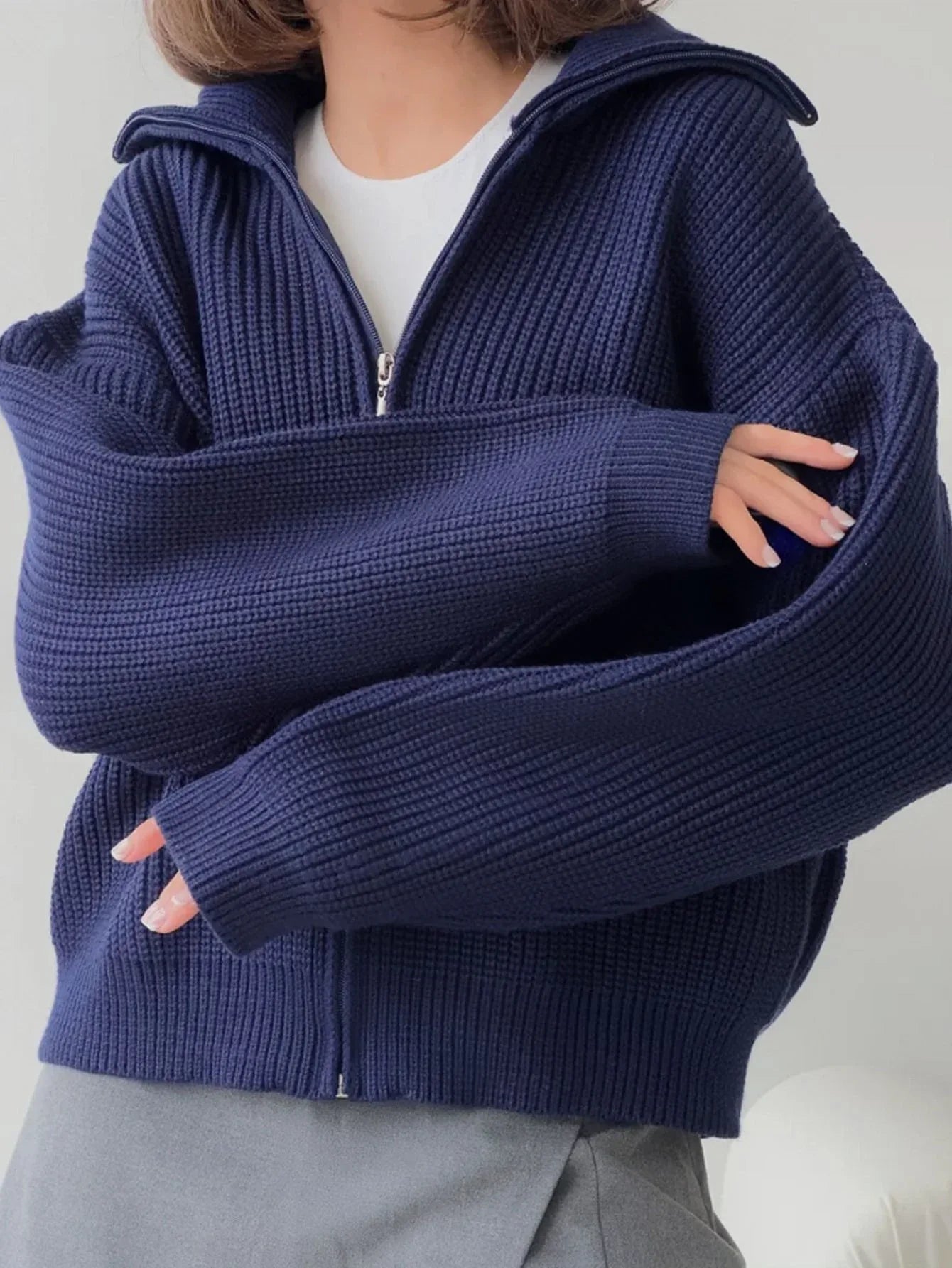 Close-up of the ribbed knit texture and oversized sleeves of a navy blue zip-up cardigan.