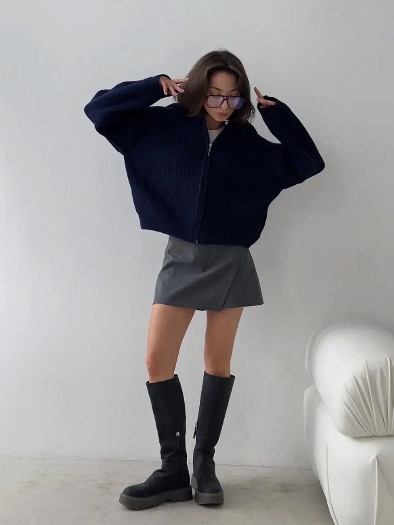 Woman wearing a navy blue oversized zip-up cardigan with a gray mini skirt and black boots.