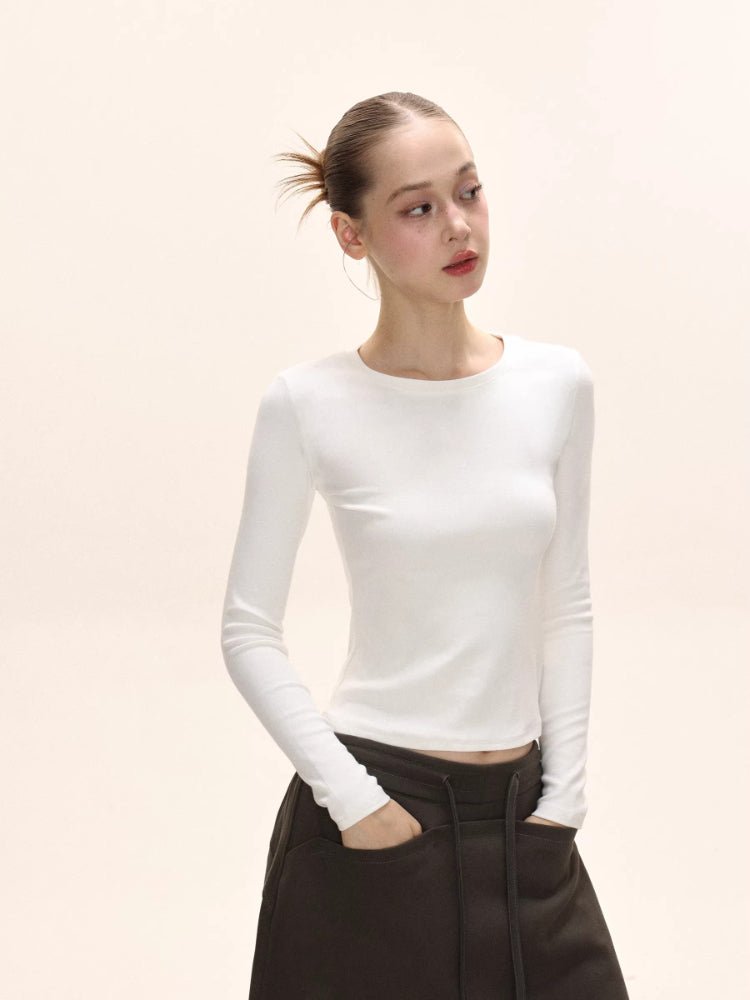 Model looking to the side in a white long-sleeve ribbed knit top and dark brown pants.