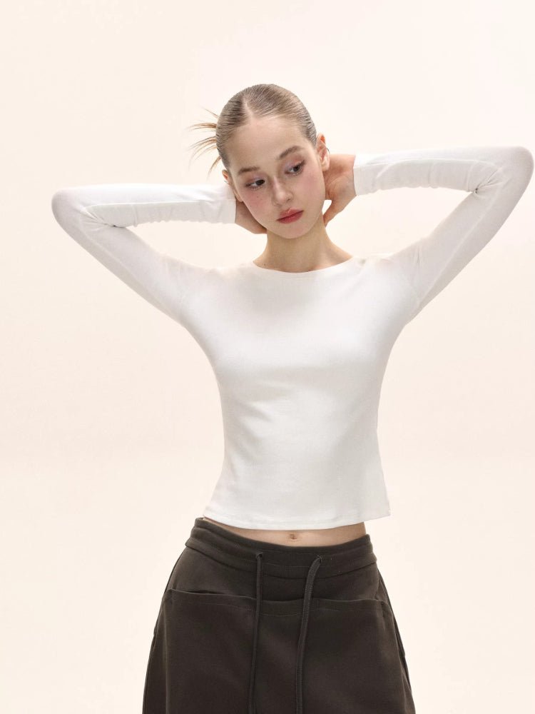 Model with hands behind head wearing a white long-sleeve ribbed knit top and dark brown pants.