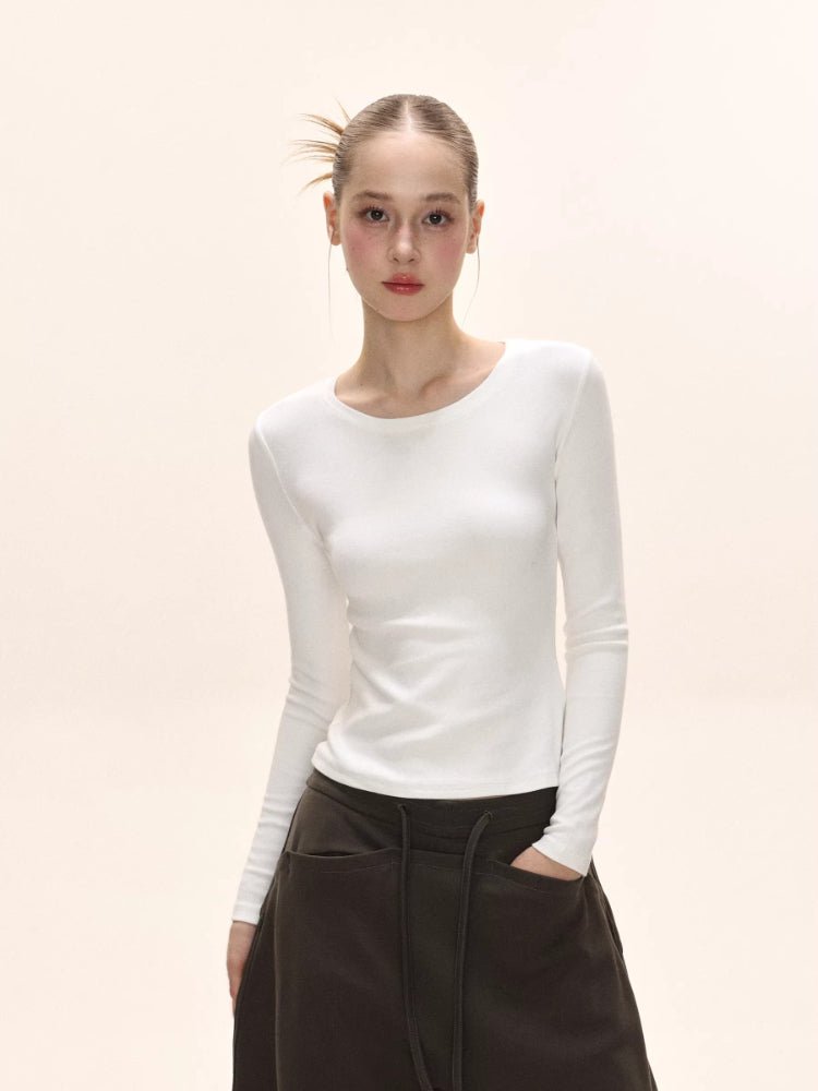 Model wearing a white long-sleeve ribbed knit top with dark brown pants.