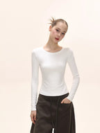Side view of a model in a white long-sleeve ribbed knit top and dark brown pants.
