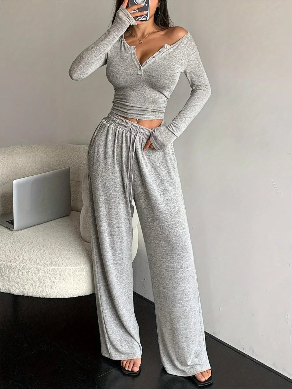 woman in a grey knit loungewear set, holding a phone and looking in a mirror