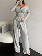 woman in a grey knit loungewear set, holding a phone and looking in a mirror