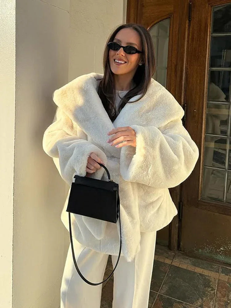 Woman wearing a white faux fur robe coat and white pants with a black handbag