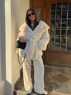 Woman wearing a white faux fur robe coat and white pants with a black handbag