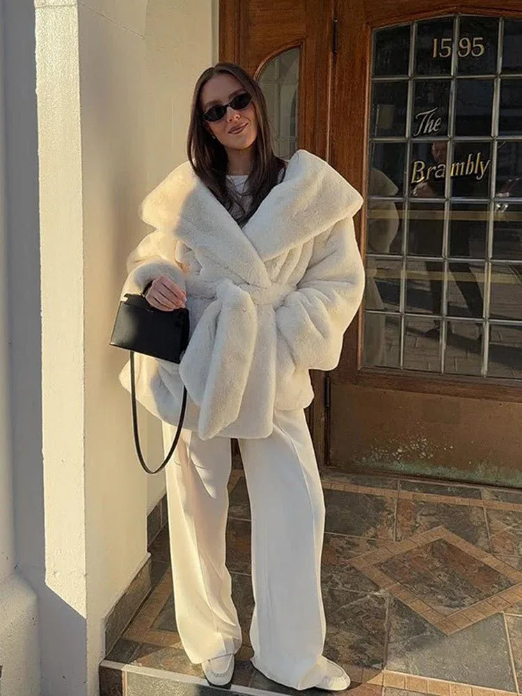 Woman wearing a white faux fur robe coat and white pants with a black handbag