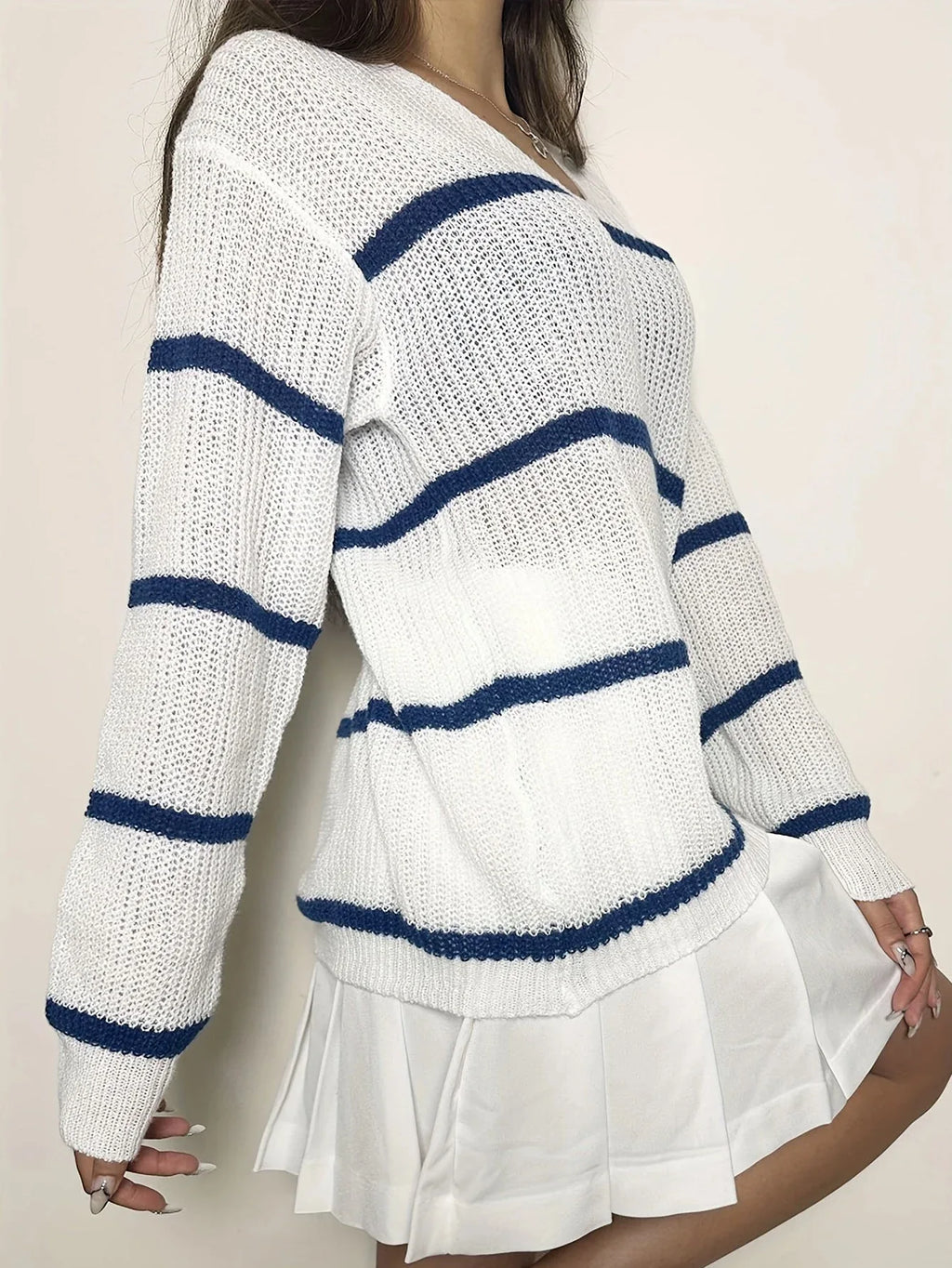 Woman wearing a white and blue striped v-neck sweater and a white pleated skirt, posing with arms crossed.