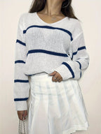 Close-up of a woman wearing a white and blue striped v-neck sweater and a white pleated skirt.