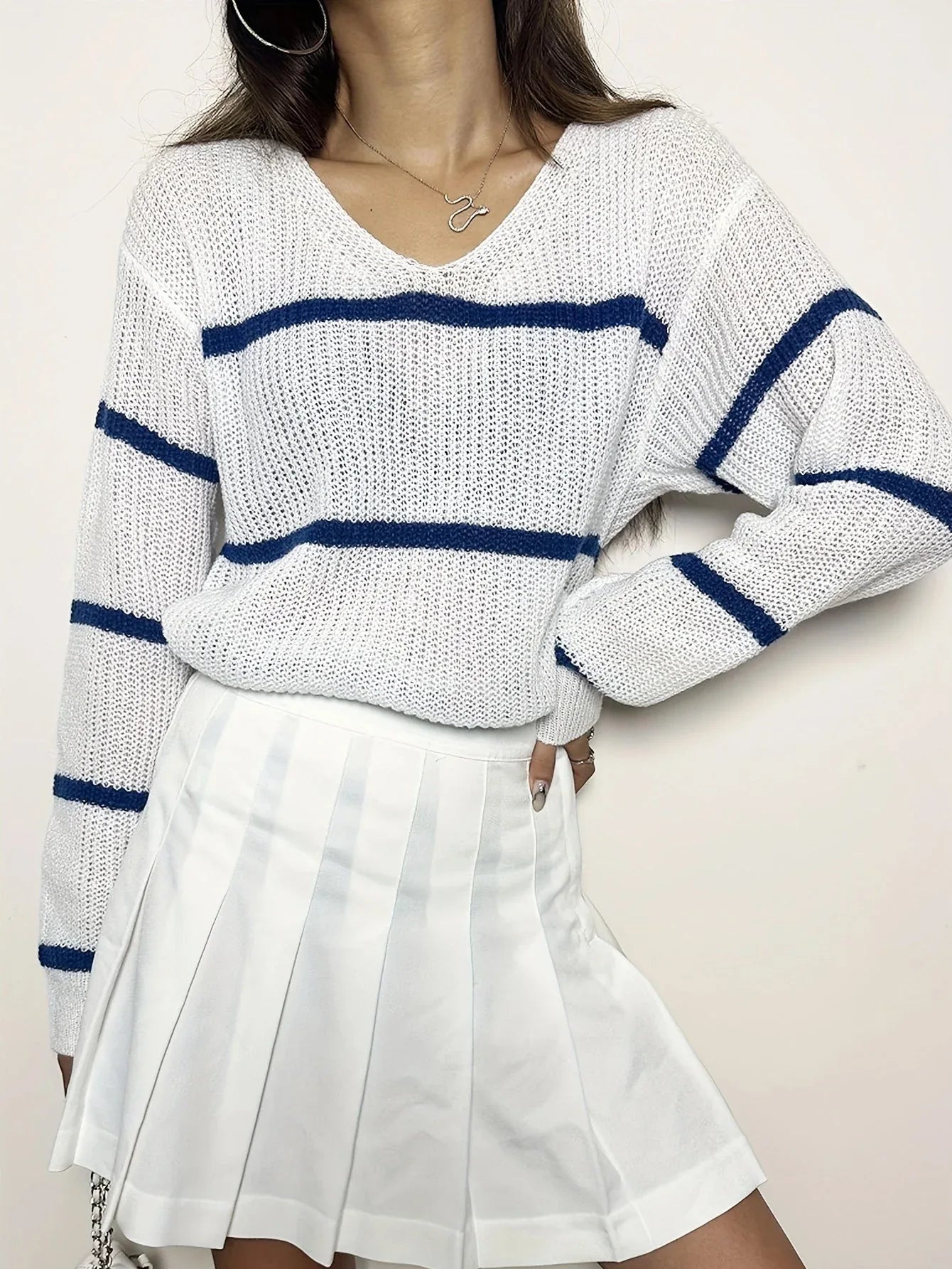 Woman wearing a white and blue striped v-neck sweater and a white pleated skirt, posing with hand on hip.