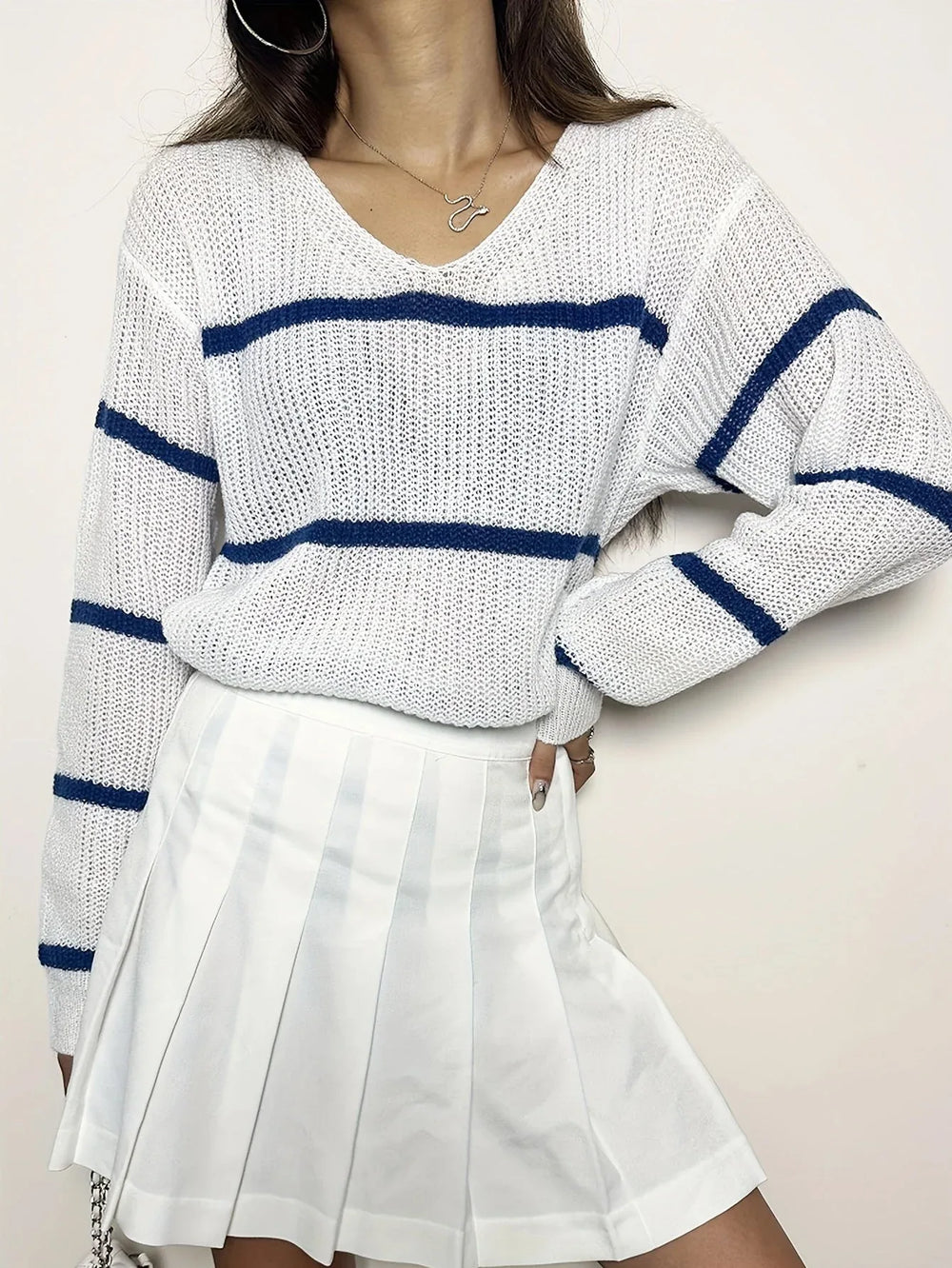Woman wearing a white and blue striped v-neck sweater and a white pleated skirt, posing with hand on hip.
