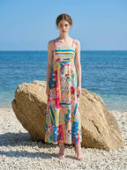 Woman wearing a colorful printed maxi dress standing on a large rock on a beach