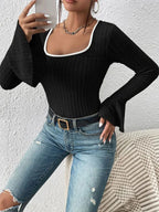 Woman taking a selfie while wearing a black ribbed long-sleeve top with a white trim square neckline and flared bell sleeves, and blue jeans.