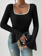 Woman holding a black handbag with a gold chain, wearing a black ribbed long-sleeve top with a white trim square neckline and flared bell sleeves, and blue jeans.