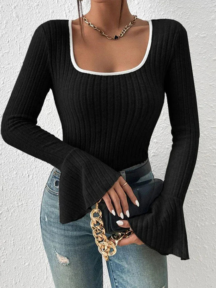 Woman holding a black handbag with a gold chain, wearing a black ribbed long-sleeve top with a white trim square neckline and flared bell sleeves, and blue jeans.