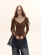 Model wearing a brown long-sleeve tie-front top and dark wash wide-leg jeans, with a brown crossbody bag.