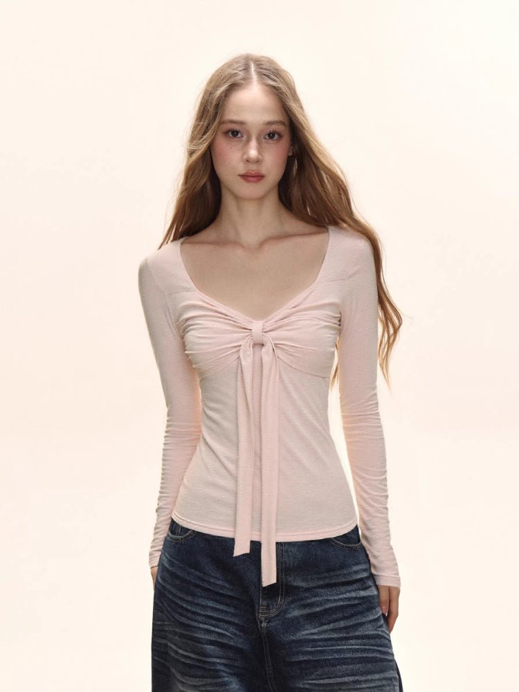 Model wearing a light pink long-sleeve tie-front top and dark wash wide-leg jeans.