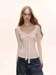 Model wearing a light pink long-sleeve tie-front top and dark wash wide-leg jeans.