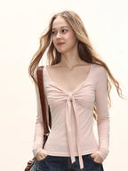 Model from the side wearing a light pink long-sleeve tie-front top and dark wash wide-leg jeans, with a brown crossbody bag.