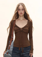 Close-up of a model wearing a brown long-sleeve tie-front top and dark wash wide-leg jeans, with a brown crossbody bag.
