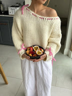 Woman wearing a cream chunky knit sweater with pink stitching details, holding a bowl of fruit.
