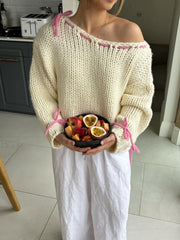 Woman wearing a cream chunky knit sweater with pink stitching details, holding a bowl of fruit.