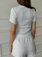 Back view of a woman wearing a white ribbed t-shirt with scalloped trim and matching white ribbed shorts with scalloped trim.