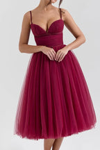 Woman wearing a burgundy tulle tea-length dress with a sweetheart neckline and ruched bodice.