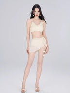 Woman wearing a cream-colored bikini set with a floral trim top and a ruffled wrap skirt, against a white background.
