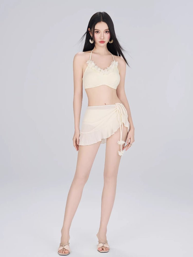 Woman wearing a cream-colored bikini set with a floral trim top and a ruffled wrap skirt, against a white background.