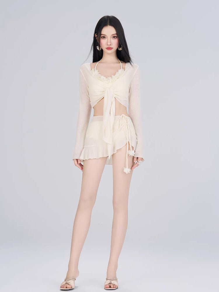 Full-body shot of a woman in a cream-colored bikini set with a sheer cover-up, standing against a white background.