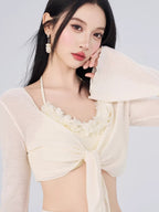 Close-up of a woman's upper body wearing a cream-colored bikini top with floral trim and a sheer, tie-front cover-up.