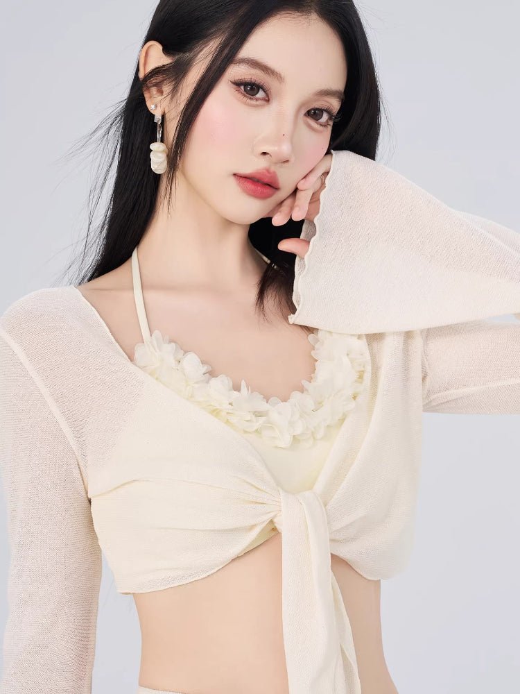 Close-up of a woman's upper body wearing a cream-colored bikini top with floral trim and a sheer, tie-front cover-up.