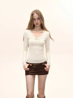 Front view of a model wearing a cream long-sleeve top with lace trim and a bow detail, and brown shorts.