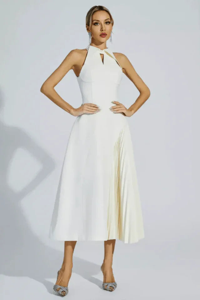 Woman wearing a white halter neck midi dress with a keyhole cutout and a pleated skirt panel, standing with hands on hips.