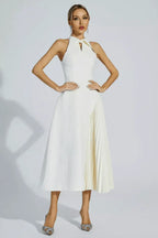 Woman wearing a white halter neck midi dress with a keyhole cutout and a pleated skirt panel, standing with hands on hips.