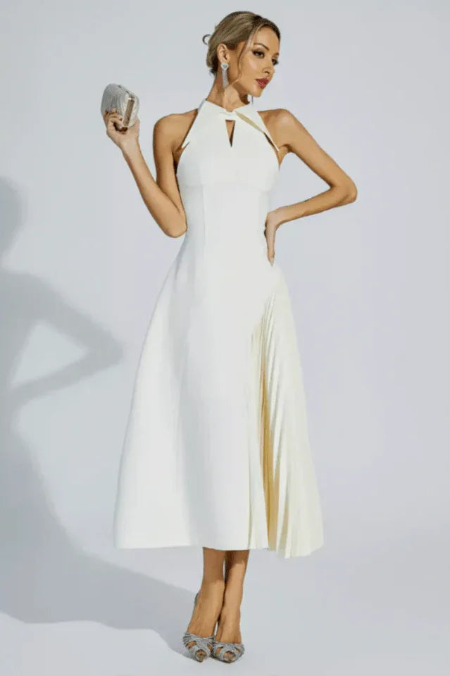 Woman wearing a white halter neck midi dress with a keyhole cutout and a pleated skirt panel, holding a clutch.