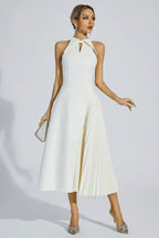 Woman wearing a white halter neck midi dress with a keyhole cutout and a pleated skirt panel, holding a clutch.