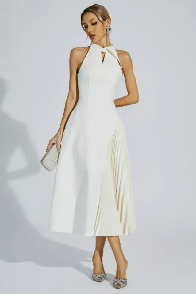 Woman wearing a white halter neck midi dress with a keyhole cutout and a pleated skirt panel, holding a clutch and posing.