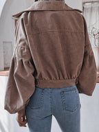 Back view of a woman wearing a brown corduroy cropped jacket with balloon sleeves and blue jeans.