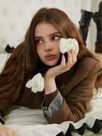 Close-up of a woman's face wearing a brown blazer and black scarf with white floral accents.