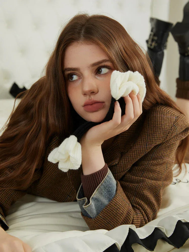 Close-up of a woman's face wearing a brown blazer and black scarf with white floral accents.