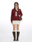 Woman wearing a burgundy v-neck sweater with a white plaid detail, a white textured mini skirt, white knee-high socks, and brown buckled boots, carrying a brown crossbody bag.