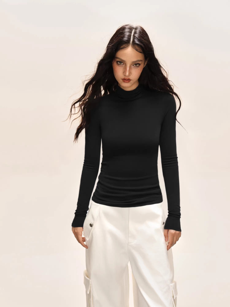 Woman wearing a black long-sleeve turtleneck top and white cargo pants, looking at the camera.