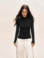 Woman wearing a black long-sleeve turtleneck top and white cargo pants, looking at the camera.