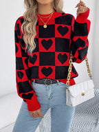Woman wearing a red and black checkerboard heart print knitted sweater with light blue jeans and a white handbag