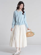 Full body shot of a woman wearing a light blue knit cardigan, white tiered maxi skirt, and holding a woven basket.