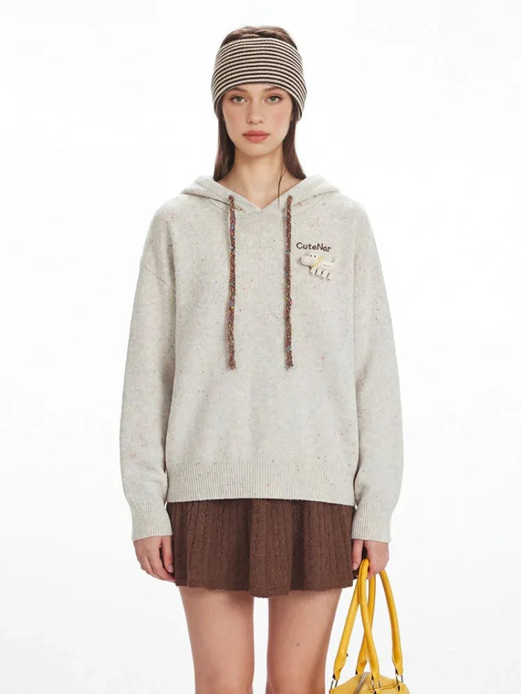Close-up of the model's upper body, showcasing the speckled knit hoodie with graphic detail on the chest and decorative drawstrings.