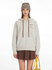 Close-up of the model's upper body, showcasing the speckled knit hoodie with graphic detail on the chest and decorative drawstrings.
