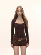 Woman wearing a brown long-sleeved top with a square neckline and bow detail, brown shorts, and a studded belt.